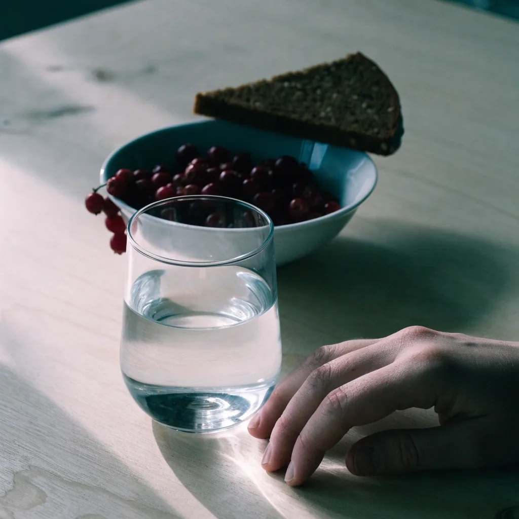 Close view of a glass of water on a birch board with one blade of morning light crossing it